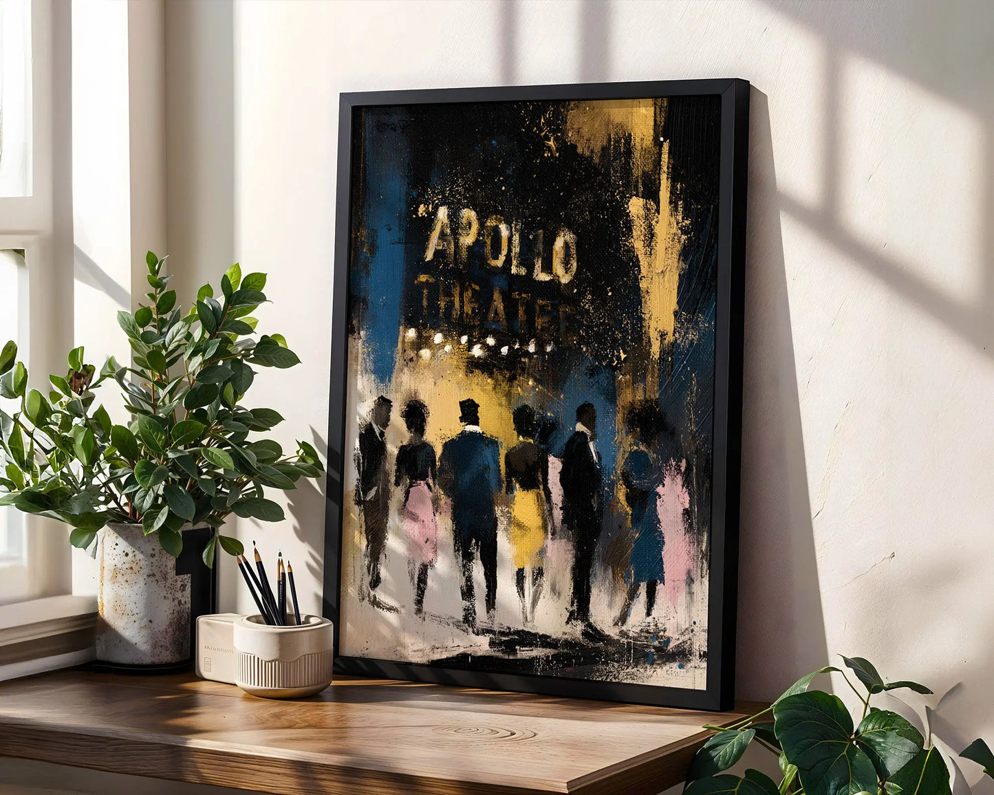 A framed art print leaning on a wooden windowsill in a bright room. The print features an abstract painting of figures walking towards the 'APOLLO THEATER' in distressed gold lettering.