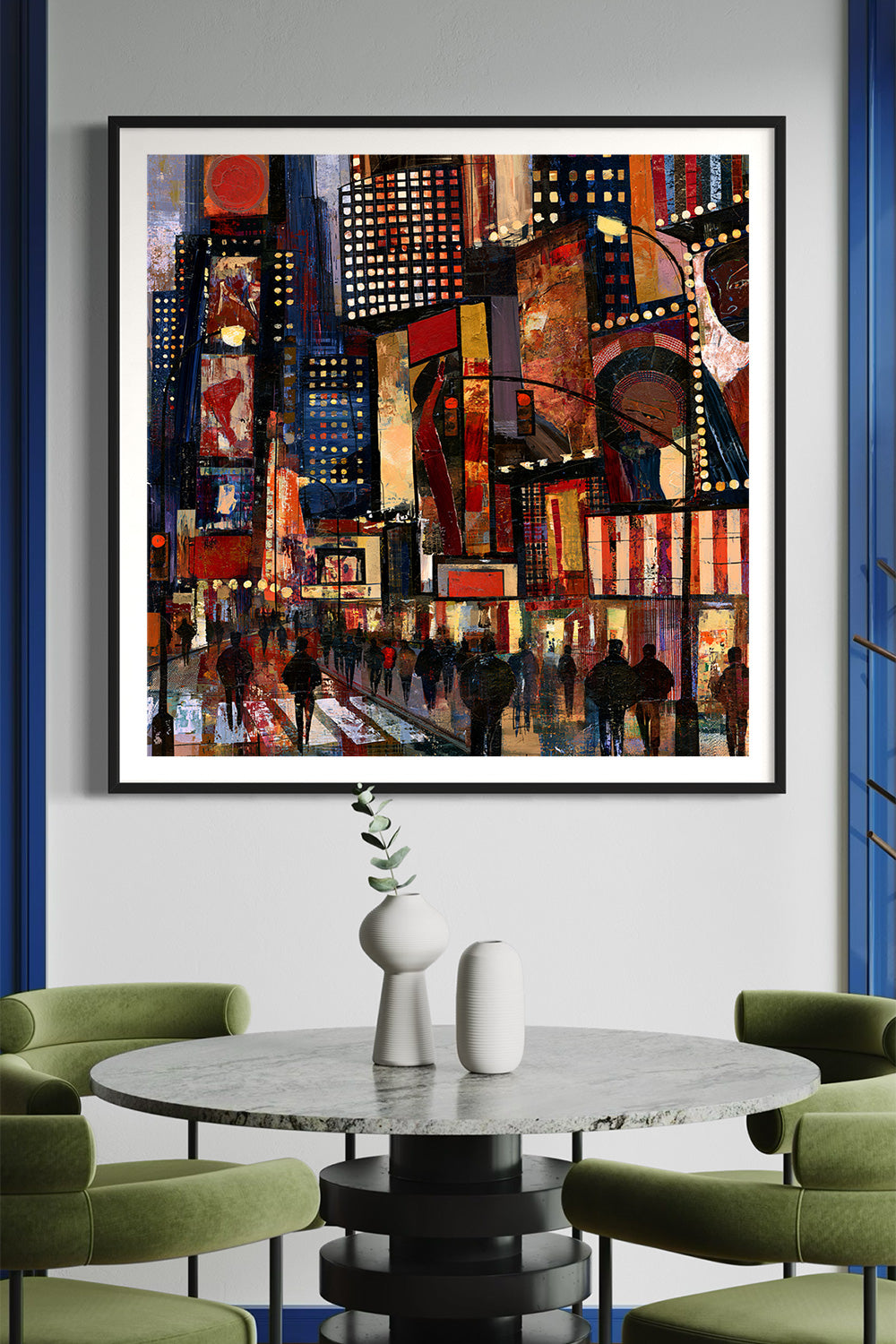 A framed abstract cityscape painting hangs on a light gray wall above a round marble-top table with green chairs. The artwork features a dense urban scene with glowing signs, pedestrians, and tall buildings in warm red, orange, yellow, blue, and black tones.