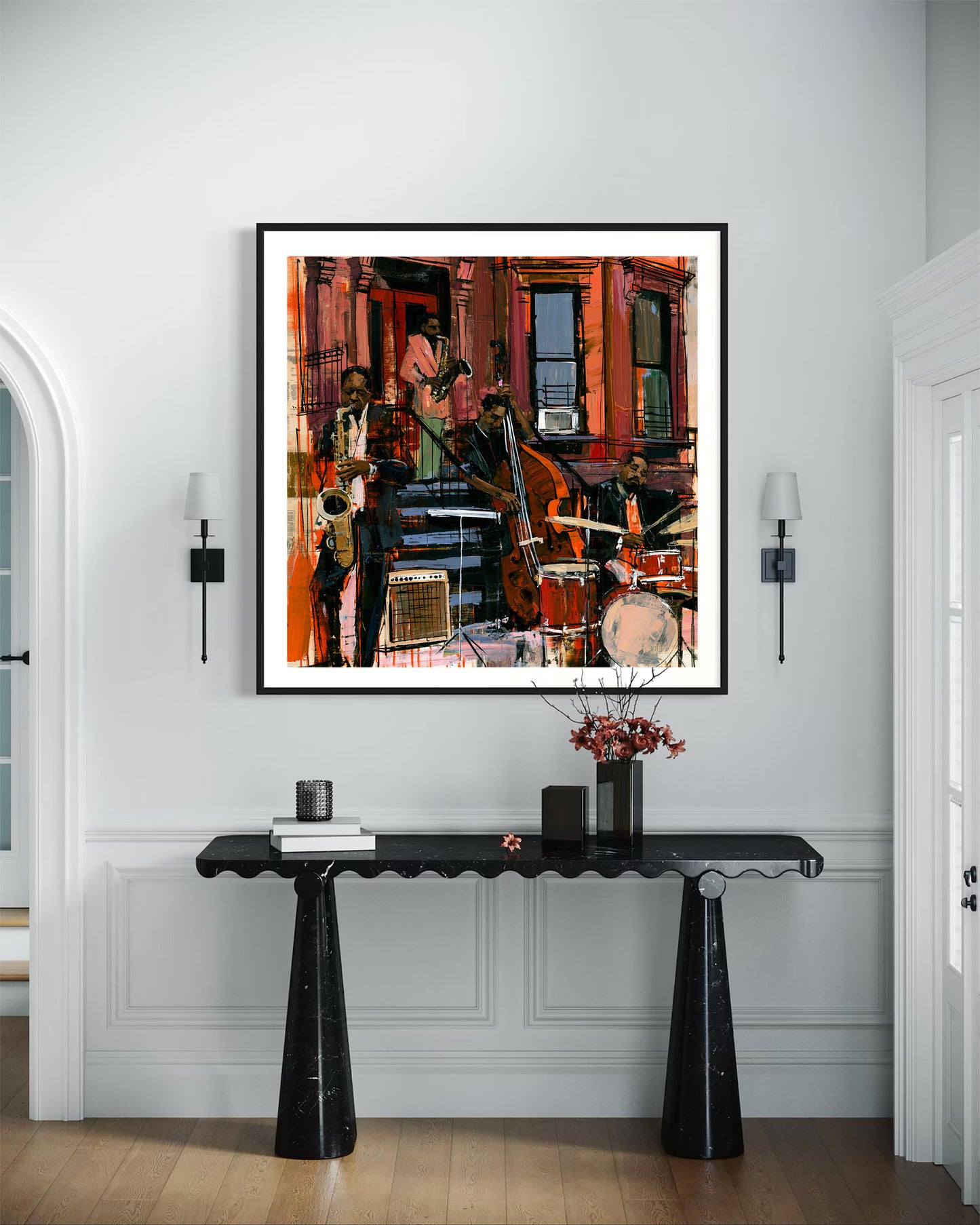 A framed square art print depicting an urban jazz band in front of red brick buildings, displayed on a white wall above a black console table in a styled interior setting.