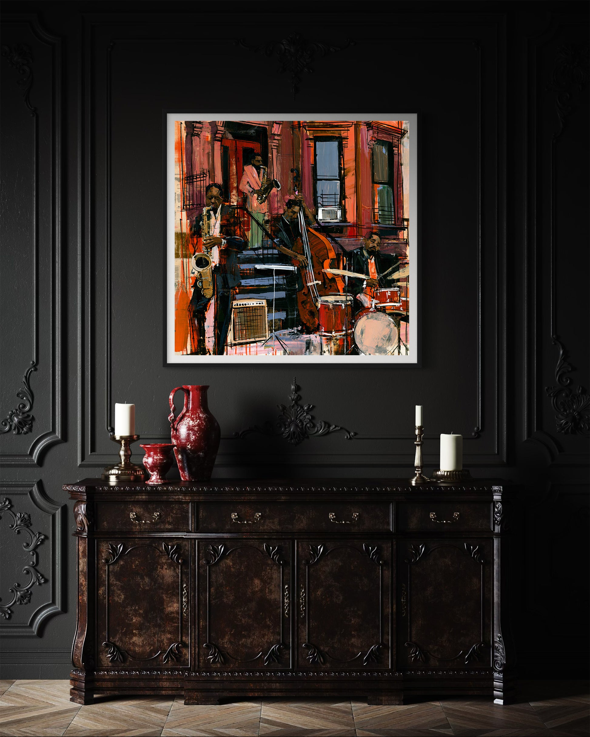 A framed abstract painting of a Black jazz musicians playing on the sidewalk  in front of historic Harlem brownstones, displayed on a dark paneled wall above an ornate dark wood console table with candles and a red vase.