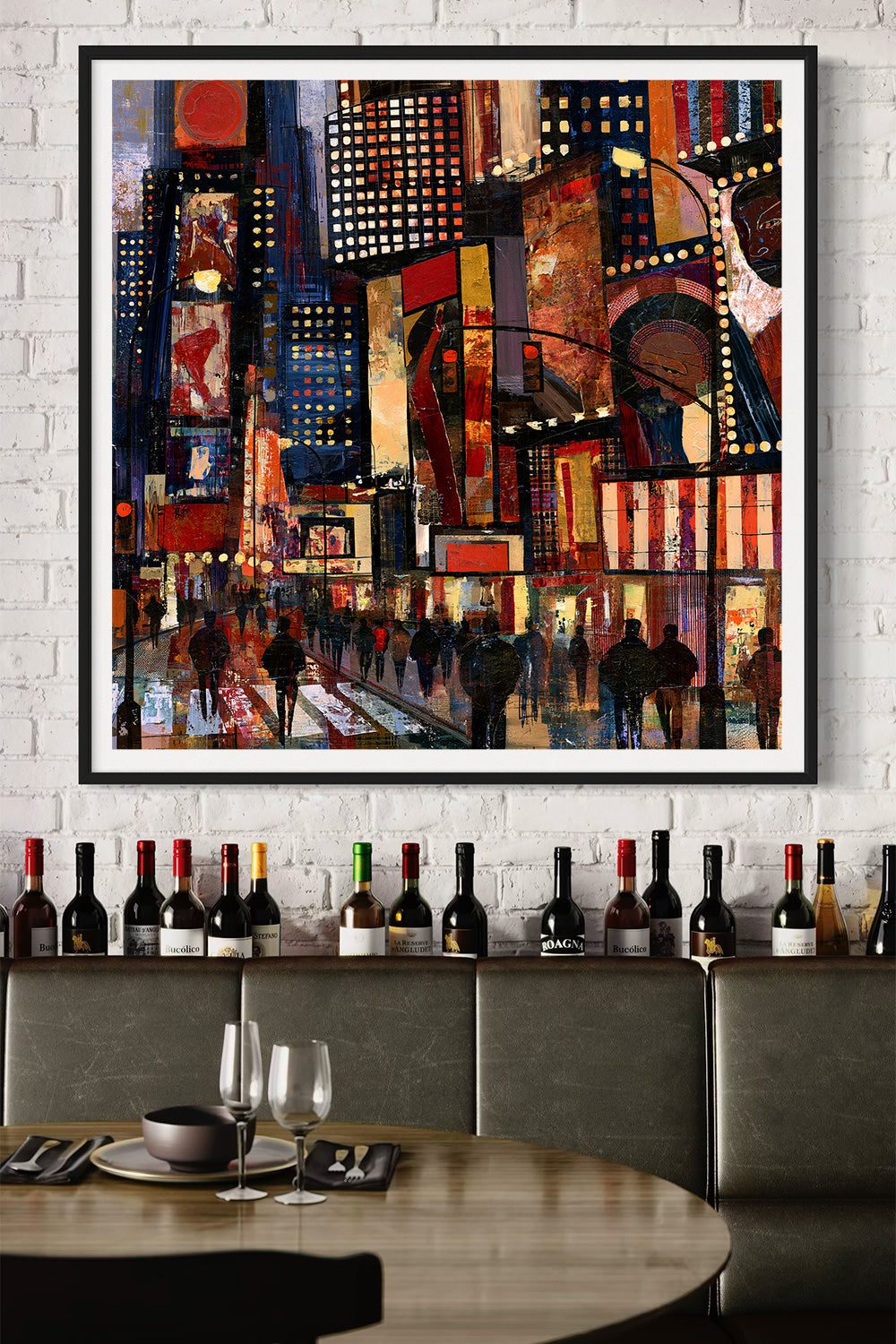 A framed abstract painting of a vibrant Times Square at night hangs on a white brick wall above a restaurant counter lined with wine bottles. The painting features a colorful, faux gritty textured cityscape with illuminated billboards, pedestrians, and a night sky, enclosed in a simple black frame.