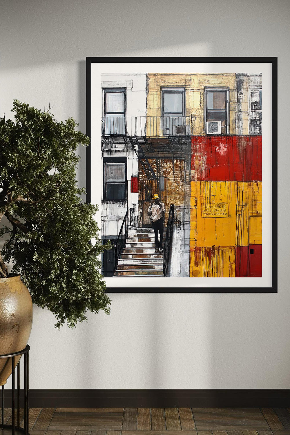 A framed abstract cityscape art print featuring brownstone buildings with fire escapes, hung on a light gray wall next to a potted green tree.