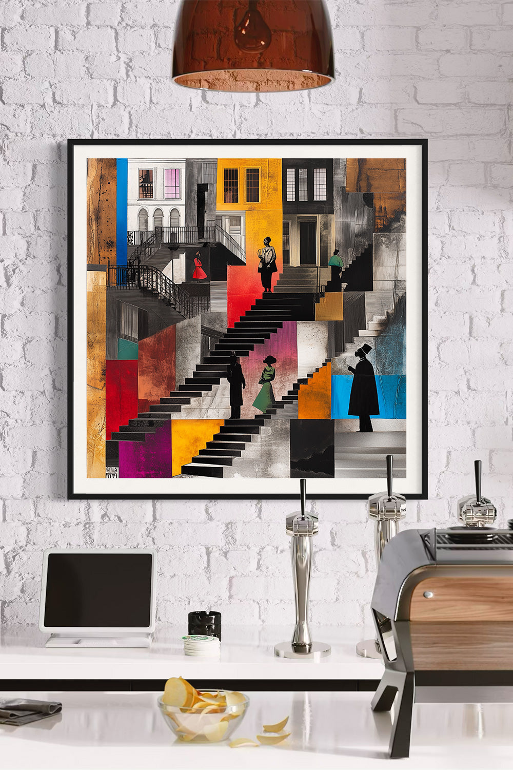 A framed abstract art print featuring a colorful geometric staircase scene with figures, displayed on a white brick wall above a kitchen counter with a laptop, coffee machine, and other decor.
